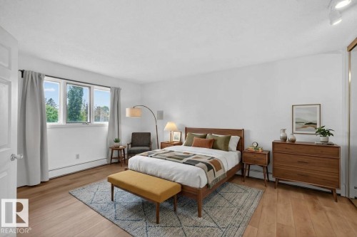 Hardwood-style flooring extends throughout this bedroom, featuring white walls and a large three-panel window - 14808 55 Street, Edmonton, AB 