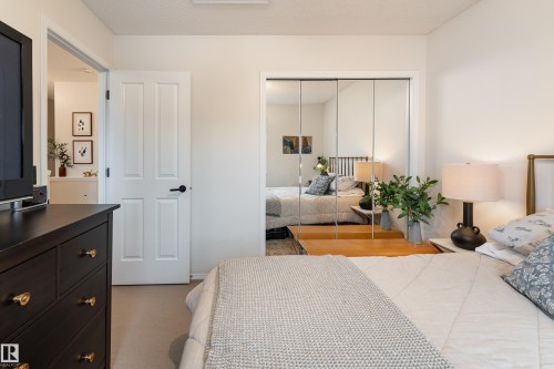 Bedroom featuring light-toned walls, neutral carpet, a white paneled door with matte black hardware, and mirrored closet doors - 5964 South Terwillegar Boulevard, Edmonton, AB 