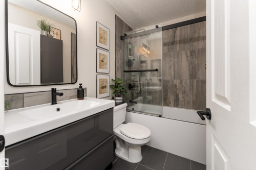 Modern bathroom featuring a single vanity with integrated sink, black hardware, a framed mirror, and a tub/shower combination with a sliding glass door - 5964 South Terwillegar Boulevard, Edmonton, AB 