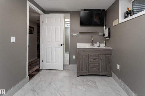 Basement bedroom with vanity area featuring a gray wood-finish cabinet, white countertop, and contemporary faucet, perfect for home-based business or teen! - 5964 South Terwillegar Boulevard, Edmonton, AB 