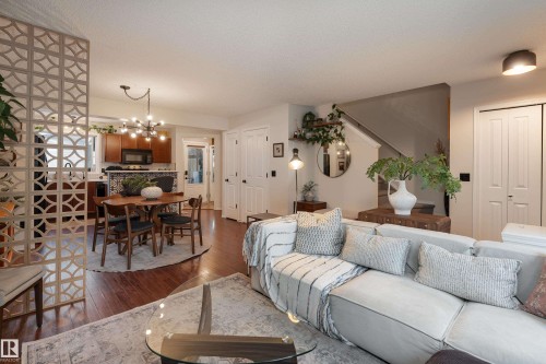 Open-concept living area featuring rich wood-finish flooring, a decorative partition wall, a dining area with a modern chandelier, and an integrated kitchen with wood cabinetry - 5964 South Terwillegar Boulevard, Edmonton, AB 