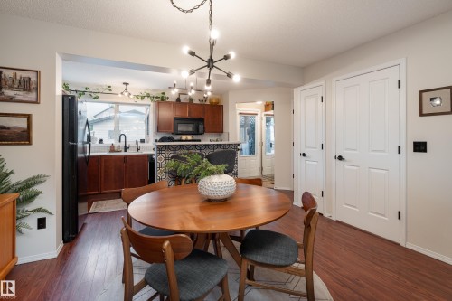 Dining area featuring wood-finish laminate flooring, a modern sputnik chandelier, and a pass-through to the kitchen with dark wood cabinetry, a tile backsplash, and a double-basin sink - 5964 South Terwillegar Boulevard, Edmonton, AB 