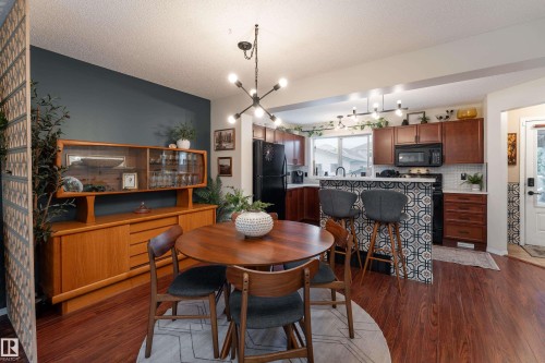 Open-concept kitchen and dining area featuring a patterned tile breakfast bar, warm colored maple cabinetry, gorgeous custom tile, and a modern chandelier - 5964 South Terwillegar Boulevard, Edmonton, AB 