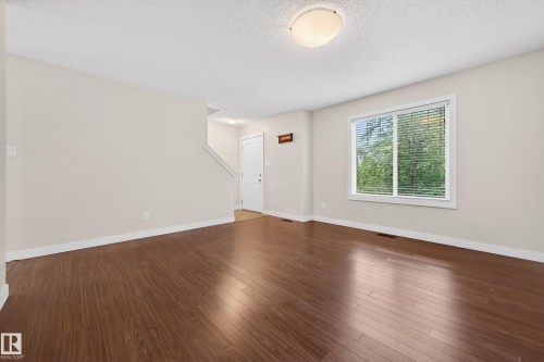 Spacious room featuring wood-finish flooring, white baseboards, and a large window with blinds - 48 8716 179 Avenue, Edmonton, AB 