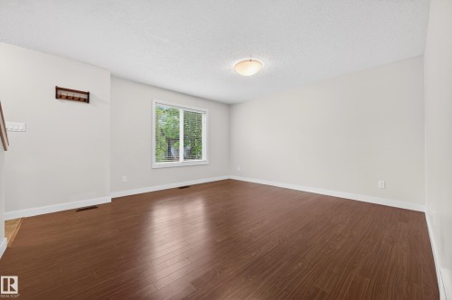 Bright interior space featuring wood-finish flooring, a window with blinds, light-toned walls, and a ceiling-mounted fixture - 48 8716 179 Avenue, Edmonton, AB 