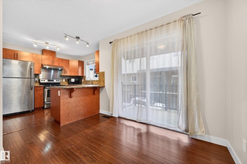Open-concept kitchen and living area featuring wood-finish flooring, warm wood cabinetry, stainless steel appliances, and a central kitchen island with seating - 48 8716 179 Avenue, Edmonton, AB 