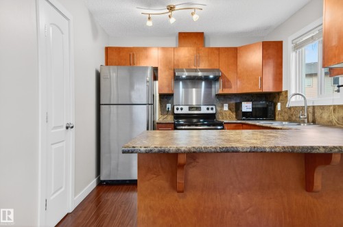 Kitchen featuring wood-finish cabinetry, stainless steel appliances, a tile backsplash, and a window above the sink - 48 8716 179 Avenue, Edmonton, AB 