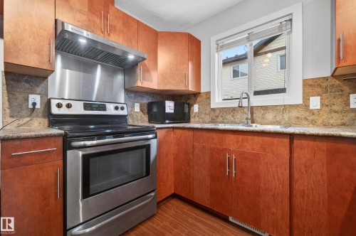 Kitchen featuring wood-finish cabinetry, stainless steel appliances, speckled countertops, a tile backsplash, and a window with blinds - 48 8716 179 Avenue, Edmonton, AB 
