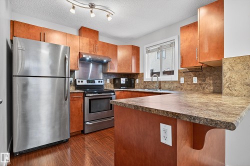 Kitchen featuring wood-finish cabinetry, stainless steel appliances, patterned countertops, and a track lighting fixture - 48 8716 179 Avenue, Edmonton, AB 