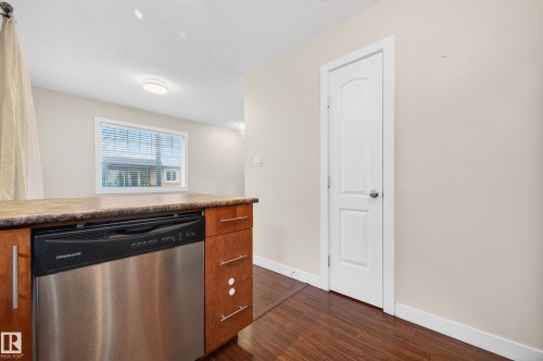 Kitchen island featuring a stainless steel dishwasher, wood-finish cabinetry with modern pulls, and a composite countertop - 48 8716 179 Avenue, Edmonton, AB 