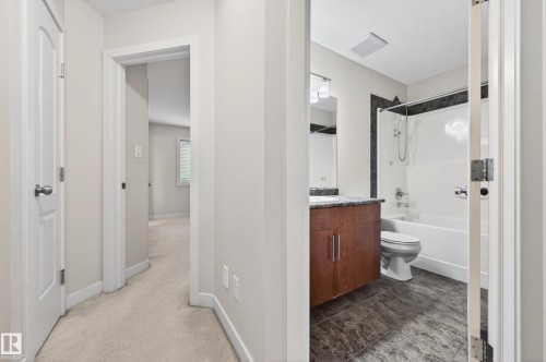 Full bathroom featuring a wood-finish vanity with a stone countertop, a white drop-in sink, and a combination shower/tub with dark stone-look tile surround - 48 8716 179 Avenue, Edmonton, AB 