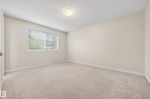 Carpeted interior room featuring neutral wall tones, a textured ceiling, white baseboards, and a window with horizontal blinds - 48 8716 179 Avenue, Edmonton, AB 
