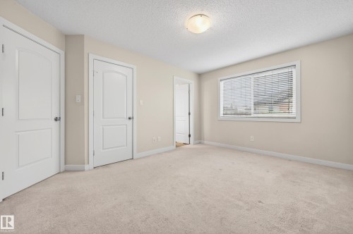 Carpeted room with a flush mount ceiling light, light-colored walls, and a large window with horizontal blinds - 48 8716 179 Avenue, Edmonton, AB 