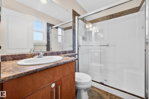 Full bathroom featuring a wood-finish vanity with a surface-mount sink, stone-look countertop, and a chrome faucet - 48 8716 179 Avenue, Edmonton, AB 