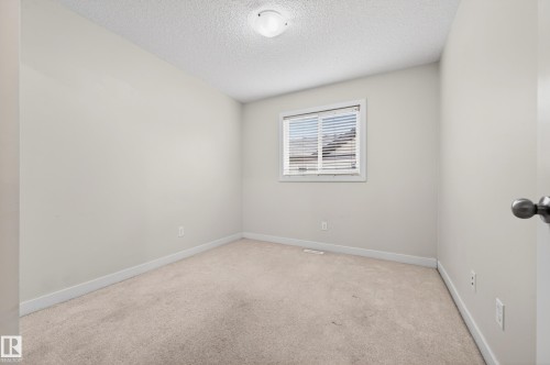 Neutral-toned room featuring a single window with horizontal blinds, light-colored carpeting, white baseboards, and a flush-mount ceiling light fixture - 48 8716 179 Avenue, Edmonton, AB 