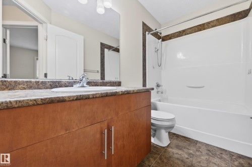 Bathroom featuring an integrated vanity sink with a mottled countertop, wood-finish cabinetry, and a white shower-over-tub combination with a tiled surround - 48 8716 179 Avenue, Edmonton, AB 
