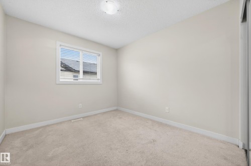 Carpeted room featuring a double-paned window with blinds, light-toned walls, white trim, and a ceiling-mounted light fixture - 48 8716 179 Avenue, Edmonton, AB 