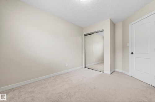Neutral-toned room featuring light-colored carpeting, a textured ceiling, and an integrated closet with mirrored sliding doors - 48 8716 179 Avenue, Edmonton, AB 