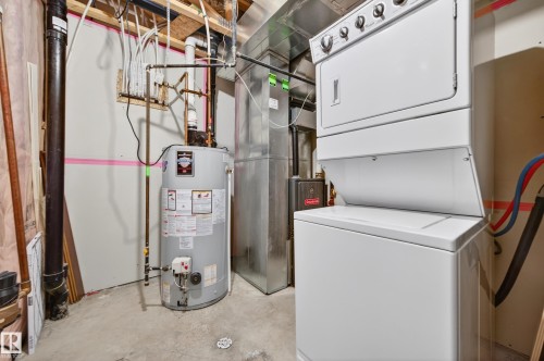 Utility area featuring a stacked washer and dryer, water heater, and exposed HVAC ductwork - 48 8716 179 Avenue, Edmonton, AB 