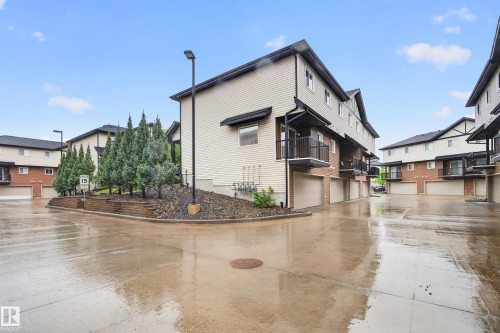 Townhome exterior featuring light-colored siding, brick accents, and a dark shingle roof - 48 8716 179 Avenue, Edmonton, AB 