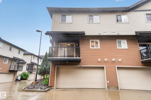 Townhome exterior featuring two-tone siding, an attached garage, a private balcony with black railings, multiple windows, and a landscaped rock garden - 48 8716 179 Avenue, Edmonton, AB 