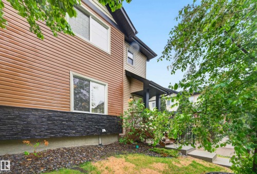 Contemporary exterior featuring horizontal siding in a warm tone, dark stacked stone detailing, and white-framed windows - 48 8716 179 Avenue, Edmonton, AB 