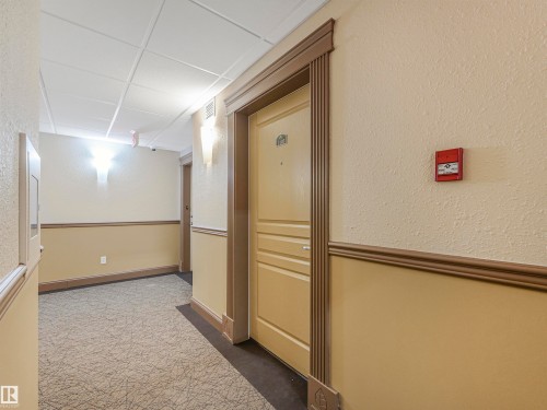 Hallway featuring a textured beige wall finish with a chair rail, wall-mounted sconce lighting, and a neutral-toned patterned carpet - 1103 2 Augustine Crescent, Sherwood Park, AB 