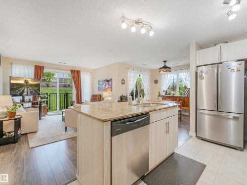 Open-concept living space featuring a central kitchen island with a granite countertop and integrated stainless steel sink, wood-finish flooring, and a sliding glass door opening to an outdoor area - 1103 2 Augustine Crescent, Sherwood Park, AB 