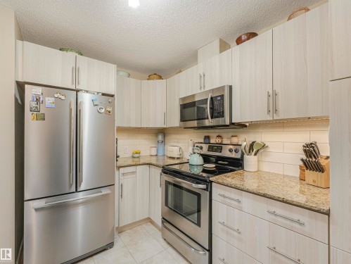 Kitchen featuring light-toned cabinetry with brushed nickel hardware, stainless steel appliances, granite countertops, and a subway tile backsplash - 1103 2 Augustine Crescent, Sherwood Park, AB 