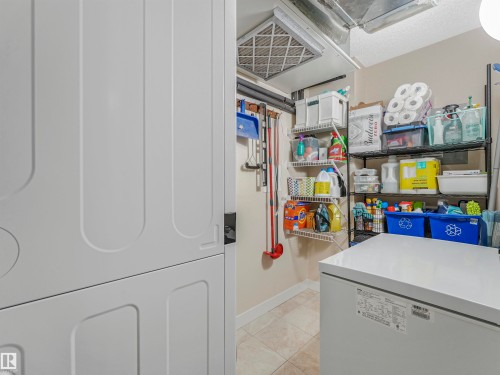 Laundry area featuring a stacked washer and dryer unit, tiled flooring, wire shelving, and an exposed ventilation system - 1103 2 Augustine Crescent, Sherwood Park, AB 