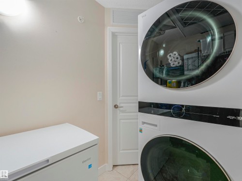 Dedicated laundry area featuring a stacked washer and dryer unit, a white chest freezer, a white paneled door, and neutral wall paint - 1103 2 Augustine Crescent, Sherwood Park, AB 