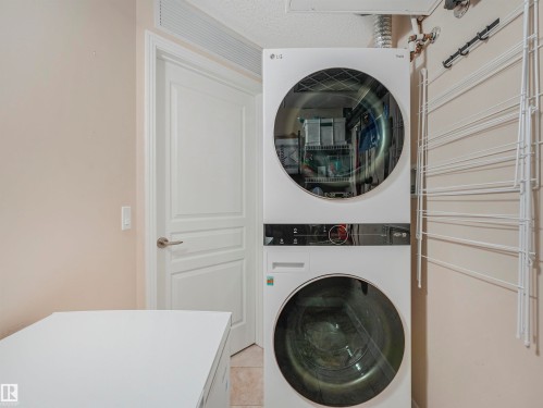 Dedicated laundry area featuring a stacked washer and dryer, tile flooring, and a solid core door with brushed nickel hardware - 1103 2 Augustine Crescent, Sherwood Park, AB 