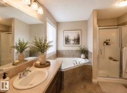 Bathroom featuring a corner soaking tub, separate glass-enclosed shower, large vanity mirror, and a single sink with a chrome faucet - 