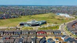 Expansive aerial perspective showcasing a residential development with numerous homes, a large central green space, a modern institutional building with solar panels, and curved roadway infrastructure - 