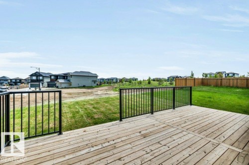 Spacious wood-finish deck with black metal railings overlooking a backyard with green space and a wooden fence - 13007 213 Street, Edmonton, AB 