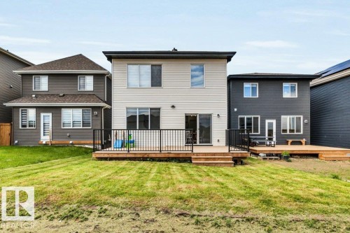 Rear exterior featuring a spacious wood-finish deck with black metal railings, a sliding glass door entry, and light-colored horizontal siding - 13007 213 Street, Edmonton, AB 
