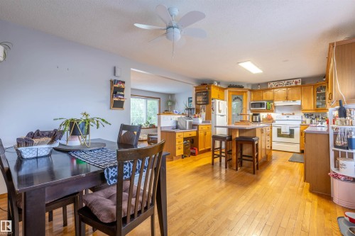 Open-concept kitchen and dining area featuring wood-finish flooring throughout, light-toned cabinetry, a central island with bar seating, and a ceiling fan in the dining space - 8902 107 Avenue, Morinville, AB 