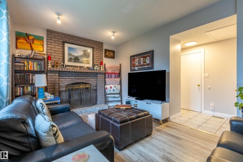 Living area featuring a brick fireplace with a stone hearth, wood-finish flooring, recessed lighting, and a white interior door - 8902 107 Avenue, Morinville, AB 