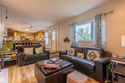 Open-concept living area featuring wood-finish flooring, a large window, and a partial wall with wood railings separating the kitchen - 