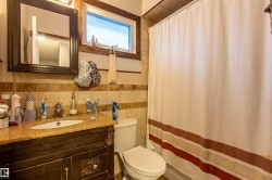 Bathroom featuring a dark wood-finish vanity with an undermount sink and a granite-style countertop, a framed mirror, a window with frosted glass, a toilet, and tiled walls - 