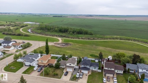 Aerial perspective showcasing a residential street with diverse home styles, bordered by expansive green fields and a winding water feature - 8902 107 Avenue, Morinville, AB 