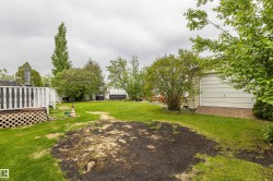 Spacious rear yard featuring an attached deck with lattice skirting, mature trees, and a detached garage with a paneled door - 