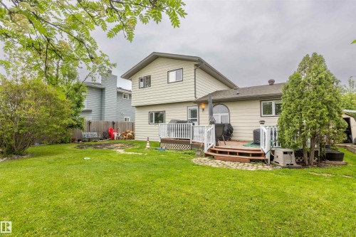 Spacious backyard featuring a multi-level wood deck with white railings, a large manicured lawn, and mature trees - 8902 107 Avenue, Morinville, AB 