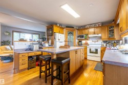 Kitchen featuring wood-finish flooring, island with seating, ample cabinetry, and white appliances - 