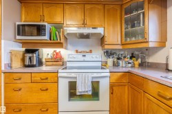 Kitchen featuring wood-finish cabinetry, a white electric range with overhead ventilation, and solid surface countertops - 