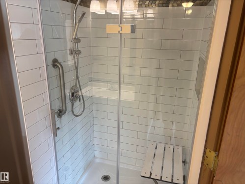 Glass-enclosed shower featuring white subway tile, built-in shelving, a fold-down bench, a grab bar, and a handheld showerhead - 51 Glenmore Crescent, St. Albert, AB 