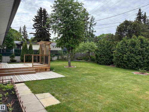 Expansive backyard featuring a large wooden deck with pergola, mature trees, manicured lawn, and concrete paver pathway - 51 Glenmore Crescent, St. Albert, AB 