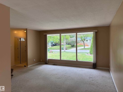 Living area featuring a large picture window, light-toned carpeting, neutral wall paint, and a textured ceiling - 51 Glenmore Crescent, St. Albert, AB 