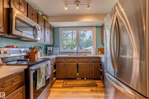 Kitchen featuring wood-finish cabinetry, stainless steel appliances, a window above the sink, and wood-look flooring - 33 Andrew Crescent, St. Albert, AB 
