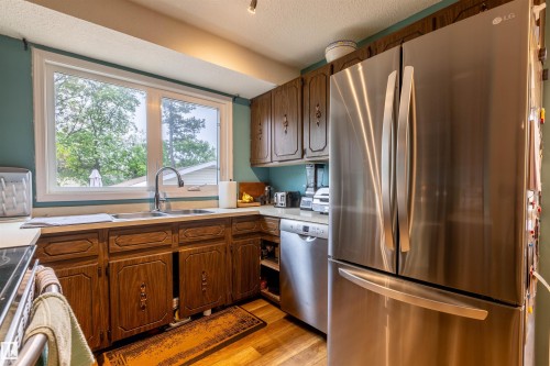 Kitchen featuring a stainless steel French door refrigerator, stainless steel dishwasher, wood-finish flooring, and a window above the sink - 33 Andrew Crescent, St. Albert, AB 